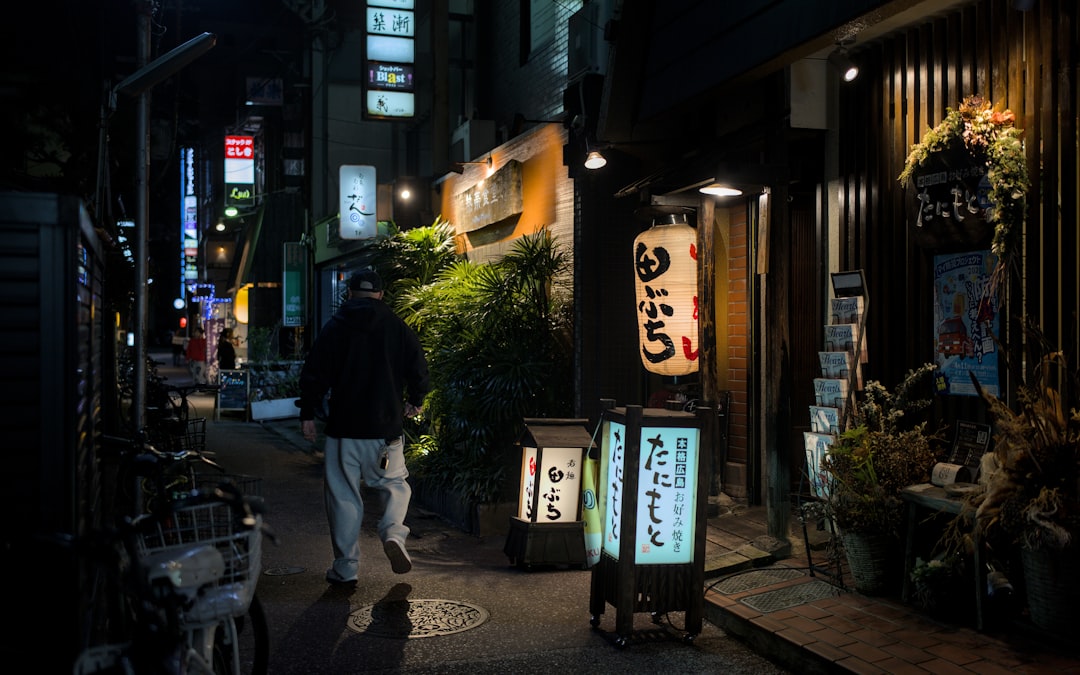 A person walks down a dark, narrow street at night.